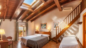 Una habitación con dos camas, suelo de madera, una escalera y un tragaluz.