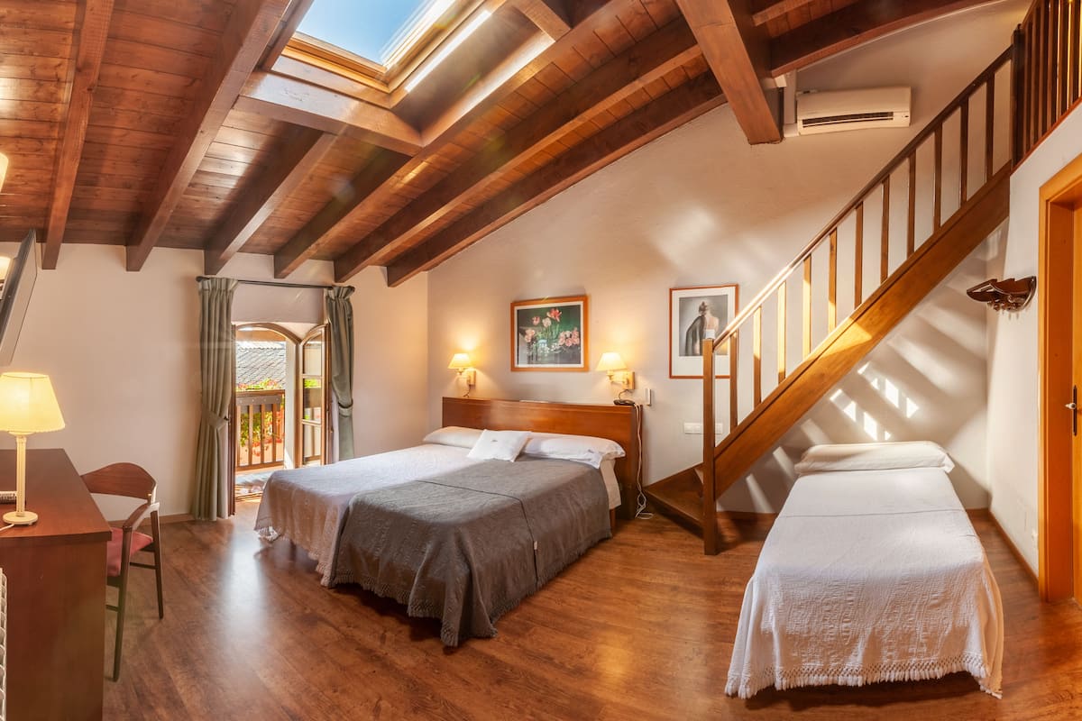 A room with two beds, wooden flooring, a staircase, and a skylight.