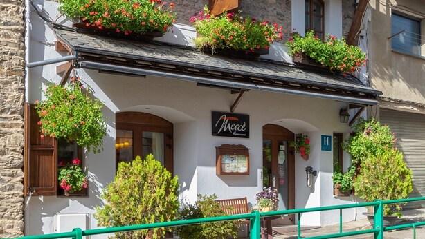 Un edificio tradicional europeo con varios balcones decorados con flores rojas, un letrero que indica un restaurante y una barandilla verde en primer plano.