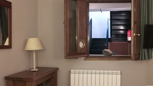 Una habitación con una mesa de madera, una lámpara, un radiador y una ventana con cortinas.