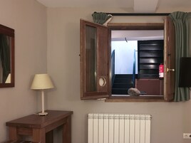 Una habitación con una mesa de madera, una lámpara, un radiador y una ventana con cortinas.