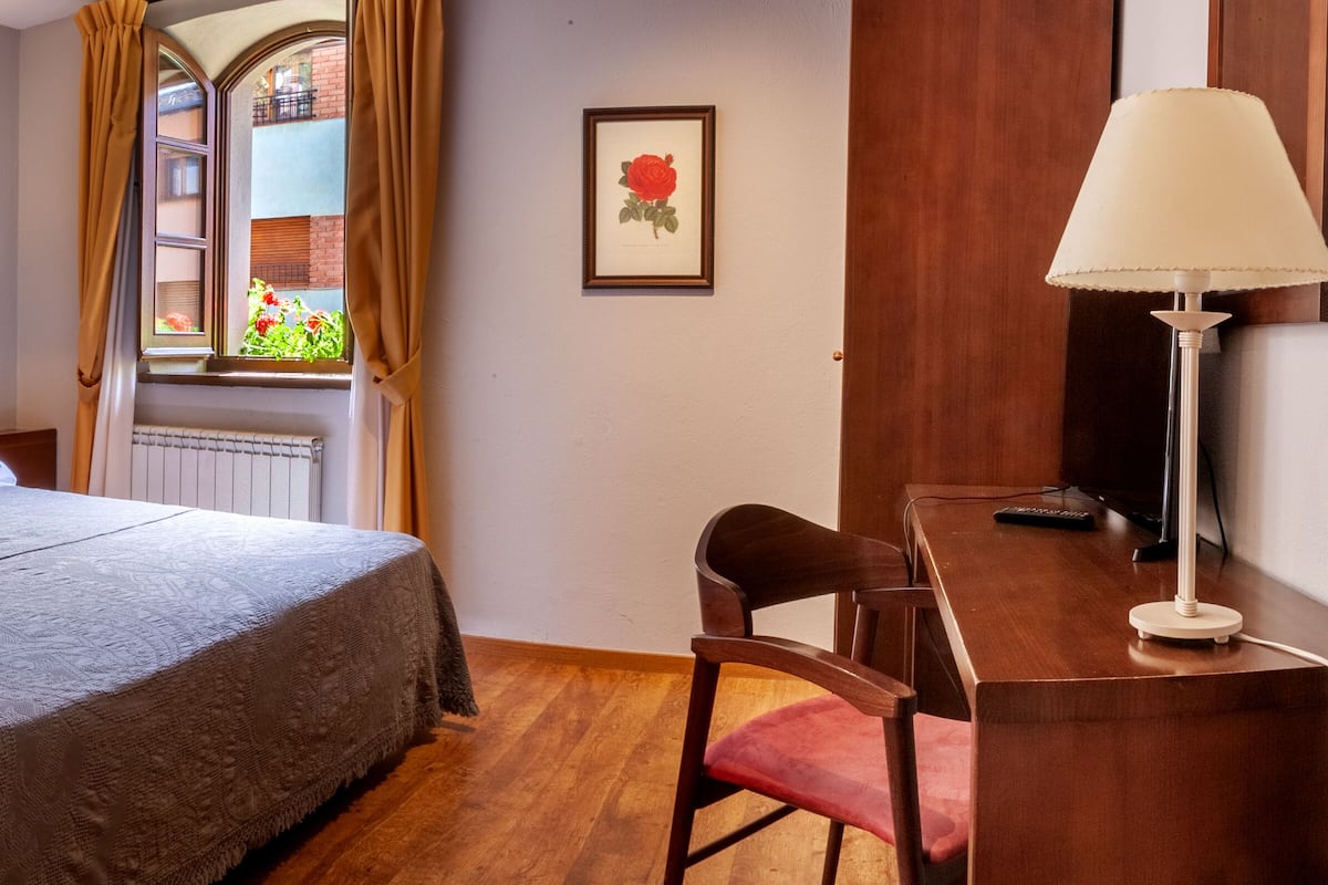 A neatly arranged hotel room with a bed, bedside lamps, a desk with a chair, and a window with curtains.