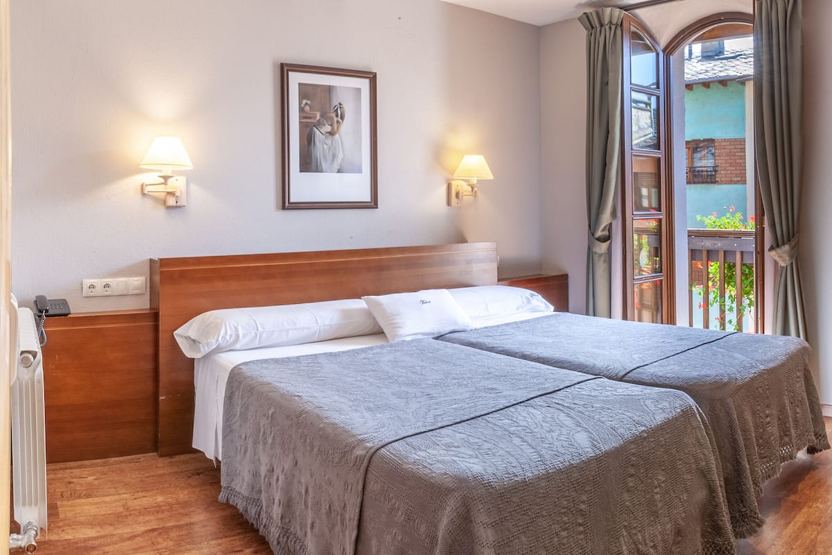 A hotel room with two beds, a desk, a chair, and a view of a balcony.
