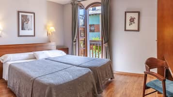 Quarto de hotel com duas camas, uma escrivaninha, uma cadeira e vista para uma varanda.