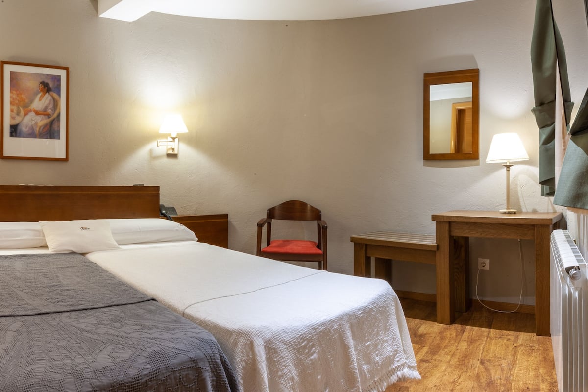 A hotel room with a double bed, two bedside tables, a chair, a desk, a mirror, and two wall-mounted lamps.