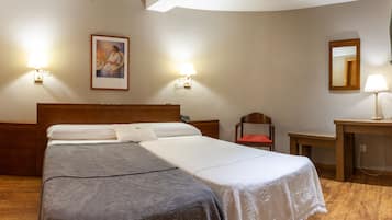 Quarto de hotel com cama de casal, duas mesas de cabeceira, uma cadeira, escrivaninha, espelho e duas luminárias fixadas na parede.