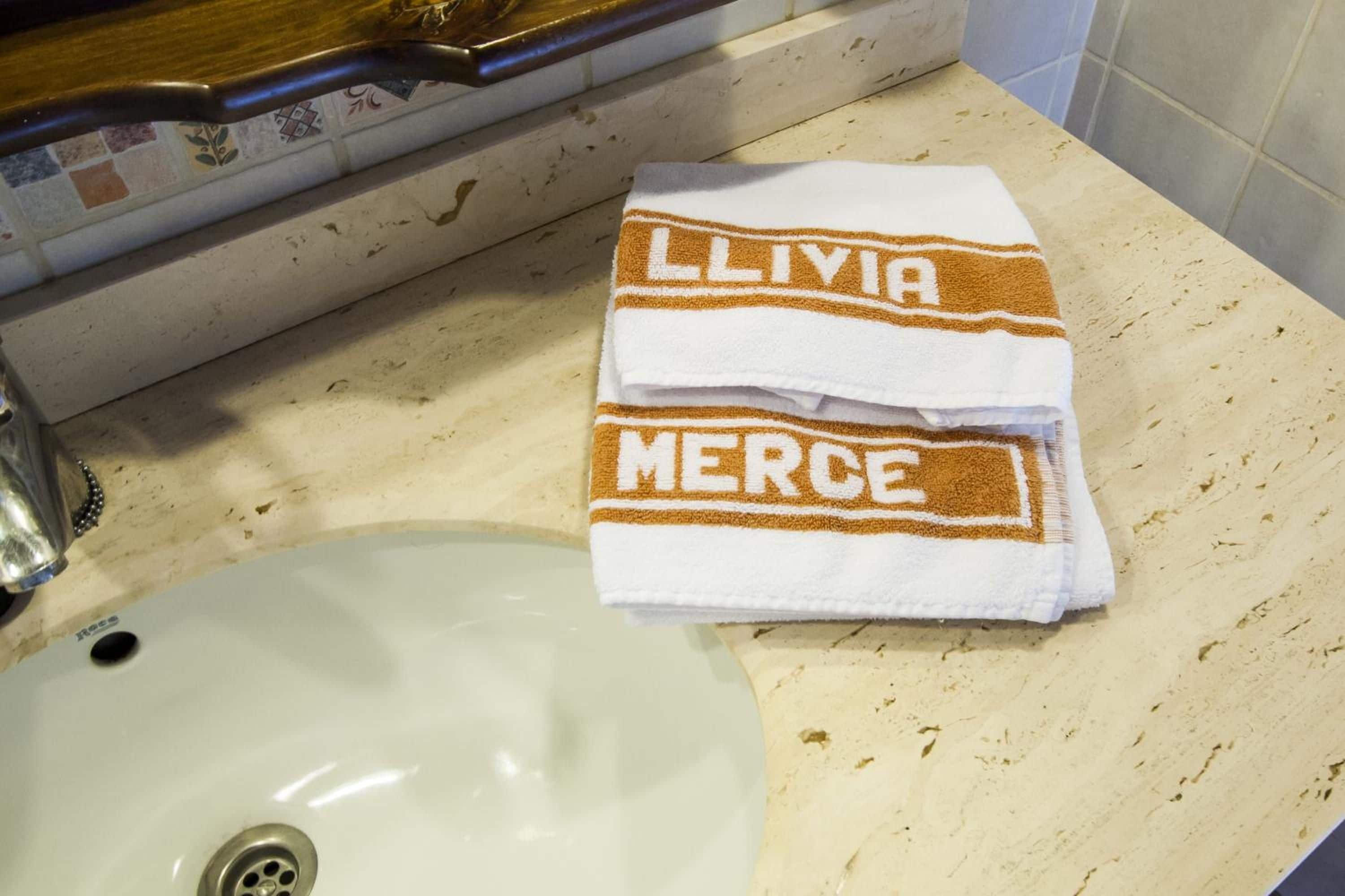 Un baño con lavamanos, una toalla con el bordado 'LLIVIA MERCE' y un salpicadero de azulejos.