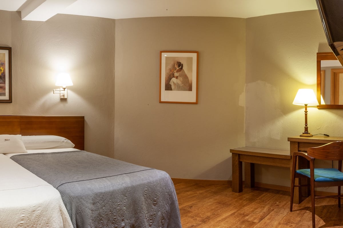 A hotel room with a bed, bedside tables, a desk with a chair, and two wall-mounted lamps.