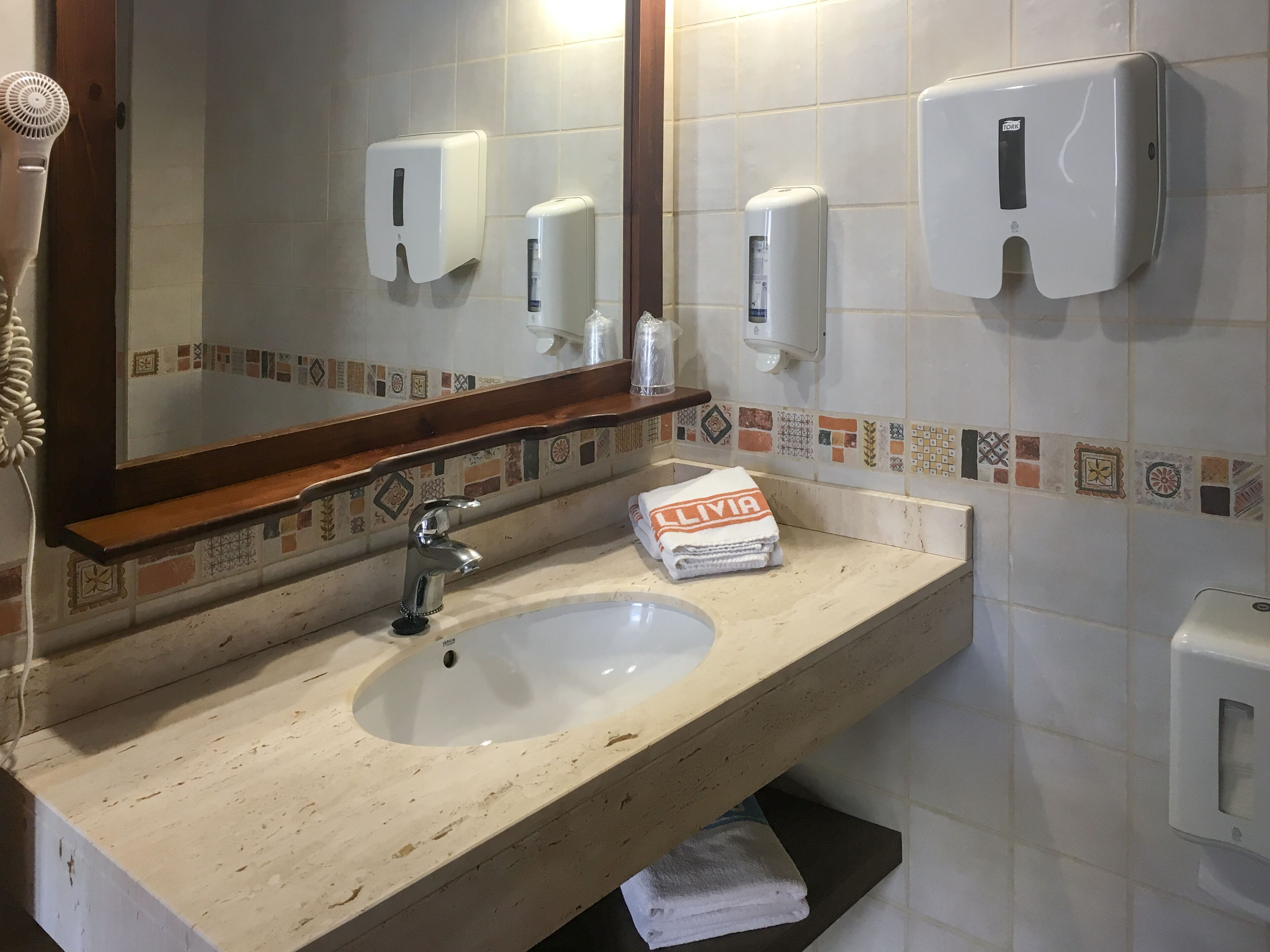 Baño con lavamanos, espejo, dispensador de toallas y secador de pelo.