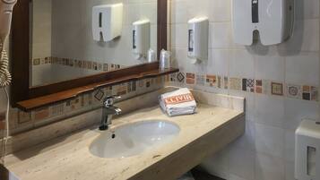 Baño con lavamanos, espejo, dispensador de toallas y secador de pelo.