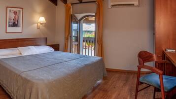 A bedroom with a wooden bed, two bedside lamps, a wooden desk with a chair, and a window with curtains.