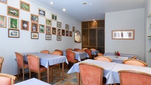 Un comedor con varias mesas y sillas, una pared decorada con cuadros enmarcados y un piso de baldosas.