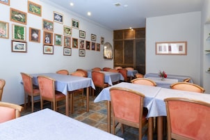 Un comedor con varias mesas y sillas, una pared decorada con cuadros enmarcados y un piso de baldosas.