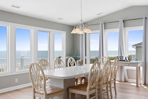 A dining room with a large table, chairs, and a view of the ocean.