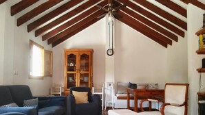 Una sala de estar con techo alto, vigas de madera a la vista, una mesa de comedor con sillas, un conjunto de sofá y un aparador con puertas de vidrio.