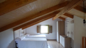 Un dormitorio con dos camas, vigas de madera, una ventana y un escritorio con lámpara.