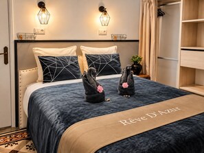 A hotel room with a bed, two wall-mounted light fixtures, a bedside table with a plant, and a wardrobe.