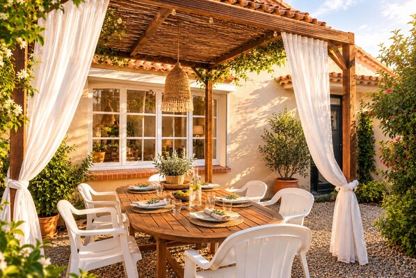 An outdoor patio with a wooden table set for dining, surrounded by white chairs, and a pergola overhead.