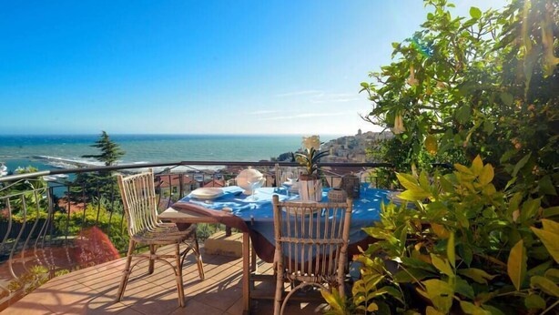 A terrace with a table set for dining, overlooking a coastal view.