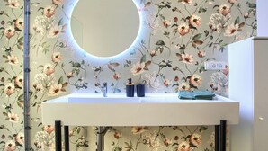 A bathroom with a round mirror, a sink, and a floral wallpaper.