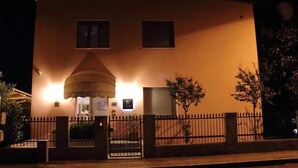 Ein Gebäude mit einer großen, beleuchteten Kuppelstruktur am Eingang, einer befestigten Auffahrt und einem Zaun mit Bäumen.