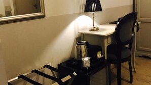 Ein kompaktes Hotelzimmer mit Schreibtisch, Stuhl und einem großen Spiegel. Auf dem Schreibtisch stehen eine Kaffeemaschine und ein Glas.