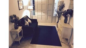 Ein Zimmer mit blauem Teppich, einem weißen Stuhl, einer dunklen Couch und einem kleinen Tisch mit Blumenvase.