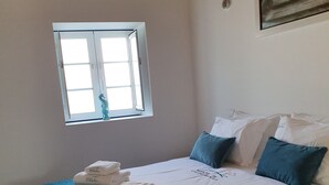 Een slaapkamer met een bed, kussens, een raam en een schilderij aan de muur.