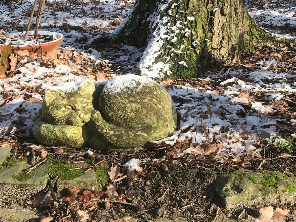 Un jardín con una escultura de piedra, un tronco de árbol y una planta en maceta.