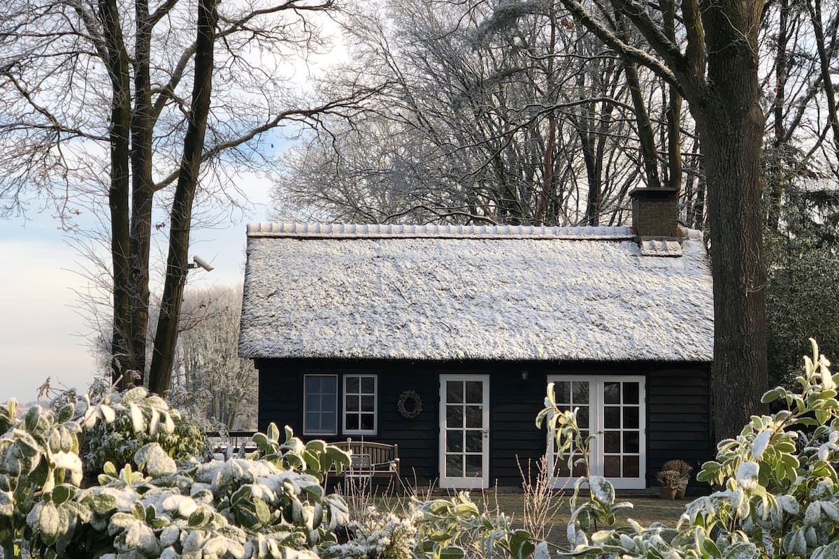 Eine rustikale Holzhütte mit einem Strohdach, umgeben von schneebedeckter Vegetation und Bäumen.
