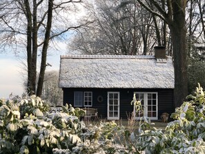 A rustic cabin with a thatched roof, surrounded by snow-covered vegetation and trees. - Hof van Eersel (Eersel)