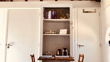 Ein Zimmer mit schrägen Wänden, Holzbalken, einer weißen Tür, einem Bücherregal, zwei Holzstühlen und einem kleinen Tisch.