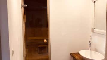 Un baño estrecho con una puerta de madera, un lavabo blanco y un espejo encima.