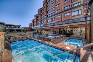 A hotel with a swimming pool, outdoor seating, and a stone wall.