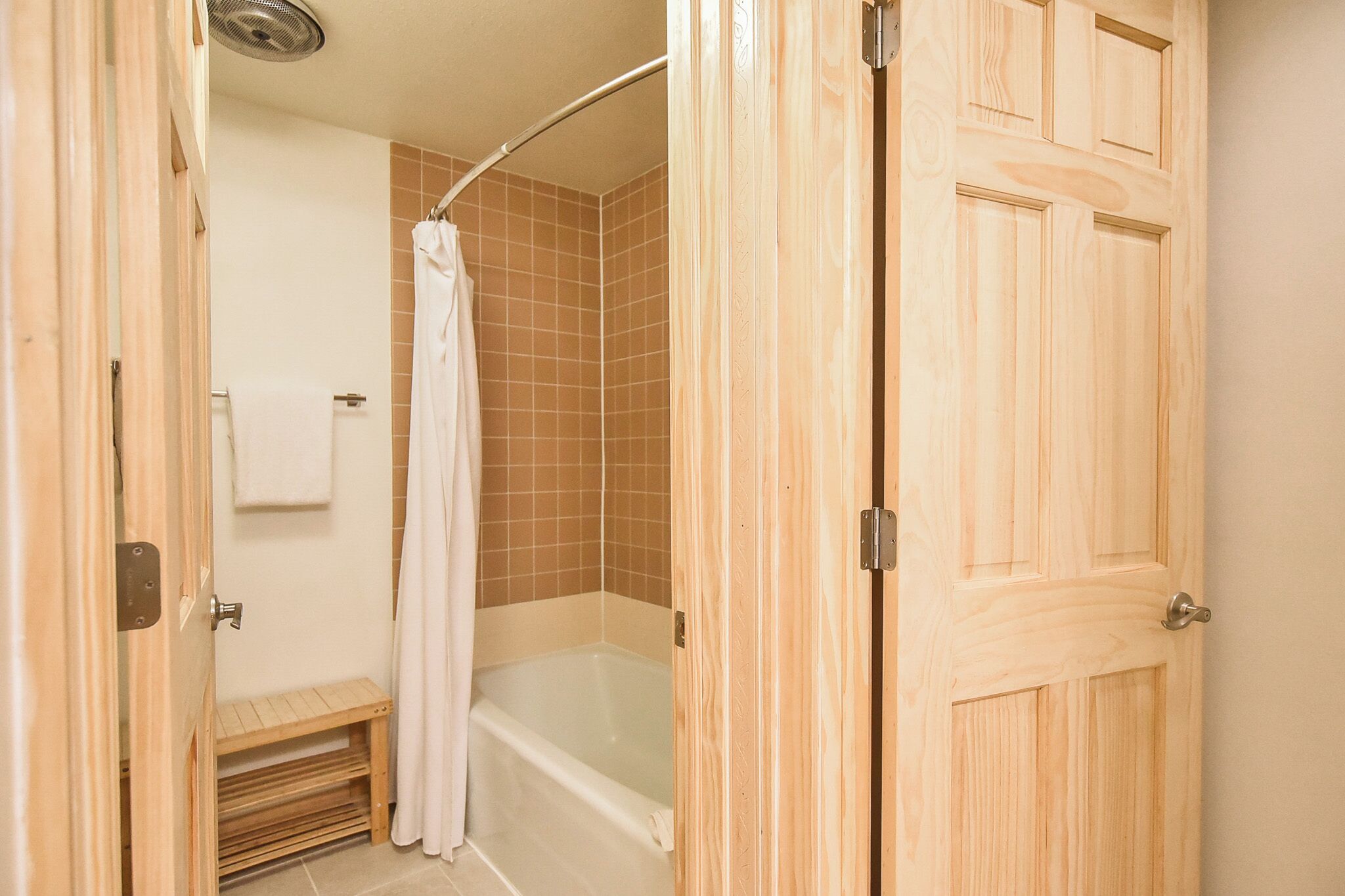 A wooden door leading to a bathroom with a bathtub, a shower curtain, and a small bench.