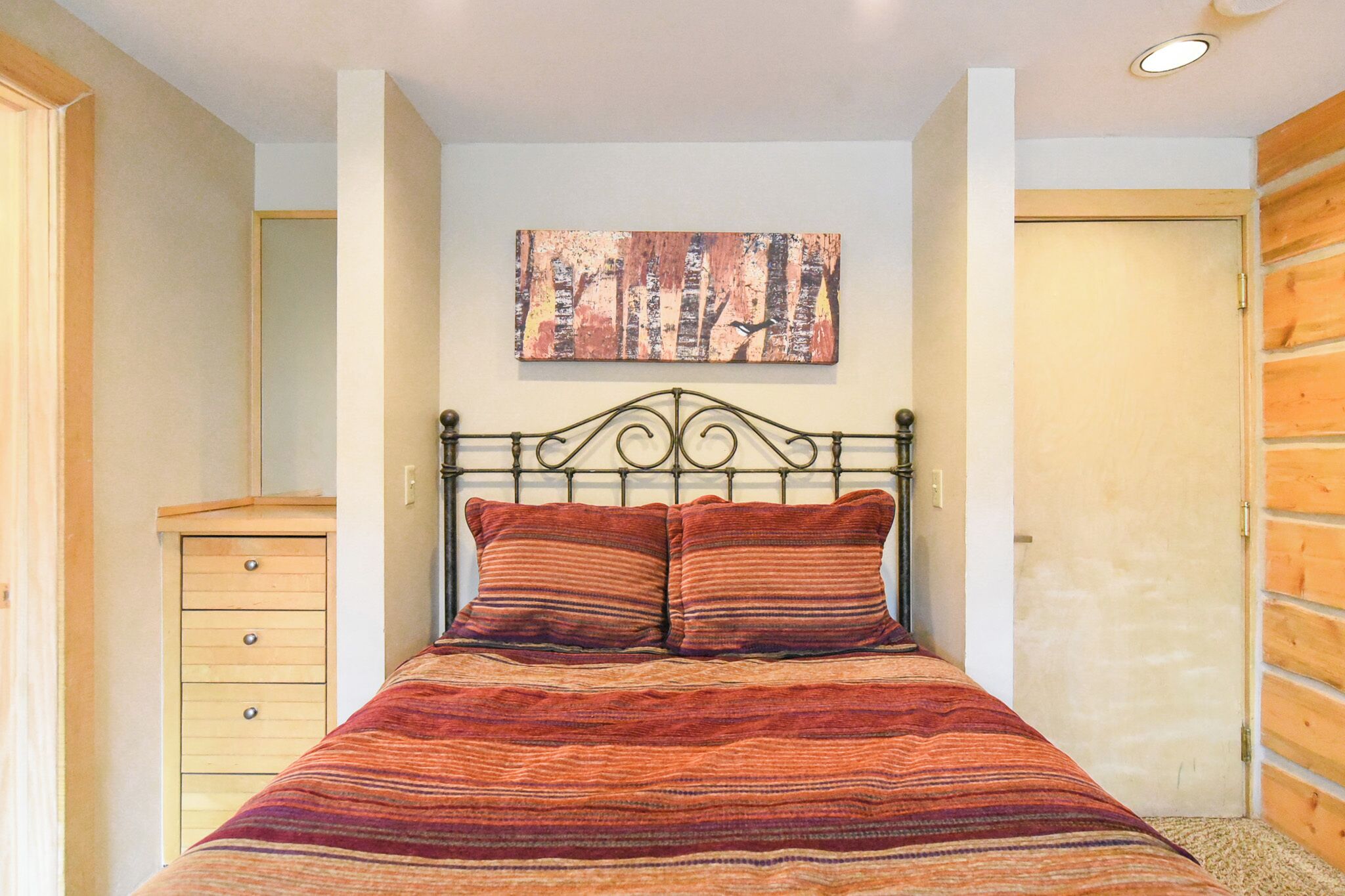 A bedroom with a bed, a wooden dresser, and a painting on the wall.