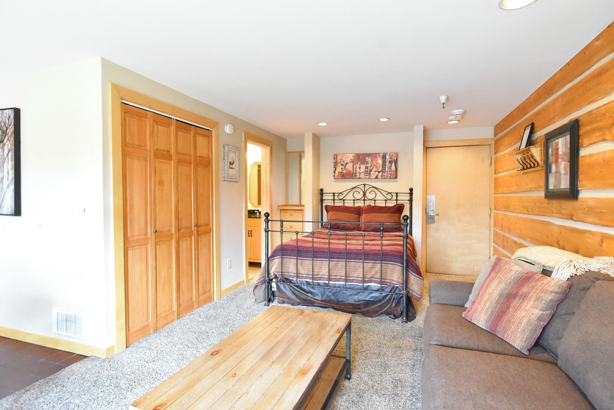 A bedroom with a bed, a wooden bench, a sofa, and a wooden wardrobe.