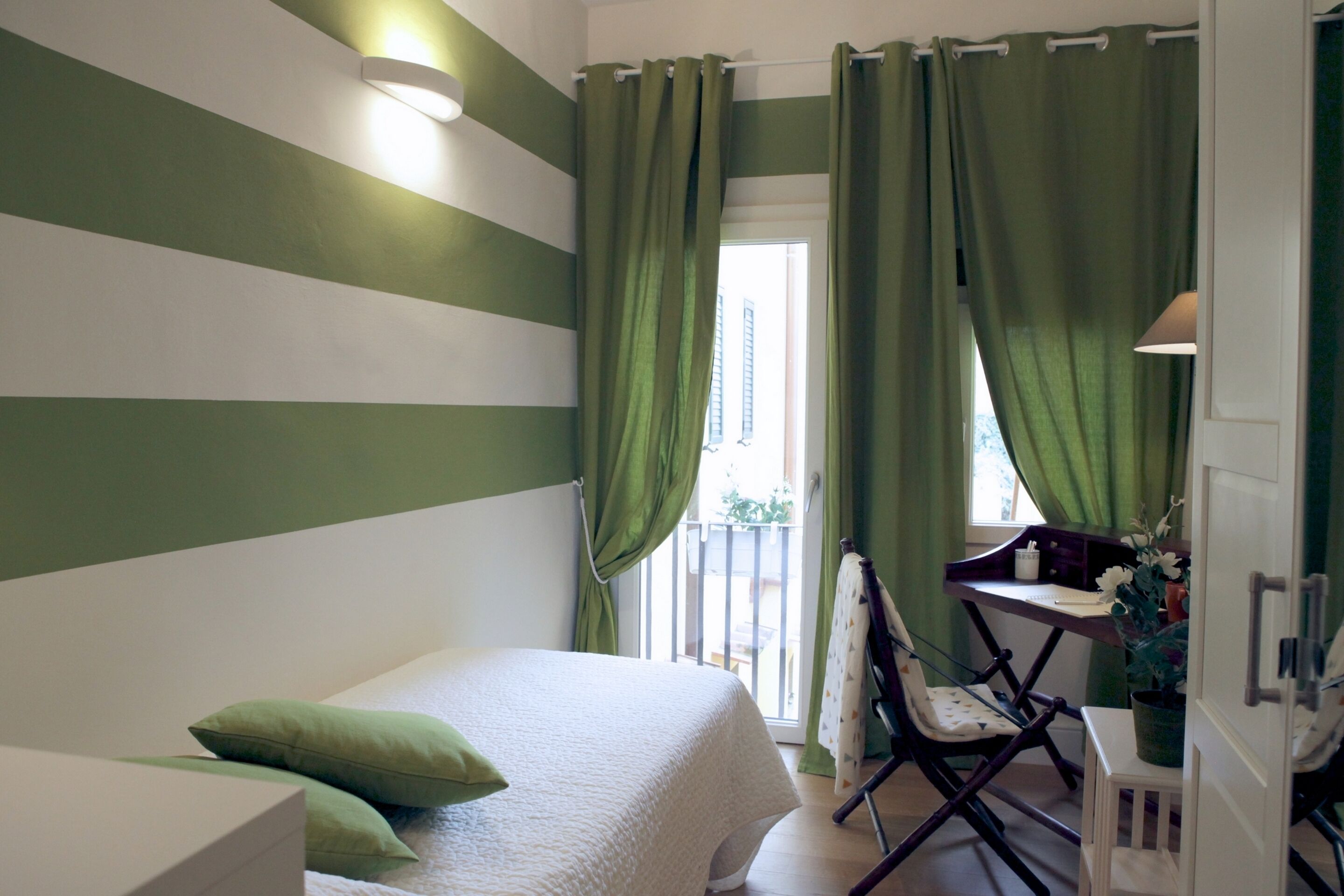 A bedroom with a bed, green curtains, a desk with a chair, and a window.