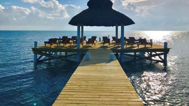 Une jetée en bois menant à une structure à toit de chaume, dotée de chaises longues.