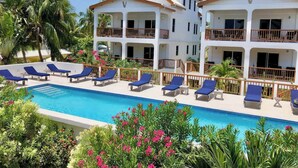 Un complexe hôtelier doté d’une piscine, de chaises longues et d’un bâtiment à deux étages avec des balcons.