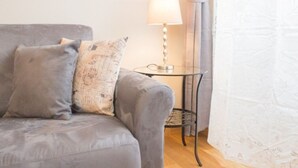 A grey sofa with two pillows, a small table with a lamp, and a patterned curtain. - Appartamento Cittadella (Florence)