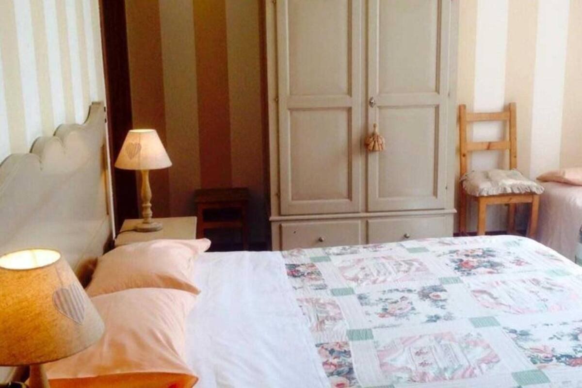 A bedroom with two beds, a wardrobe, a chair, and a nightstand with a lamp.