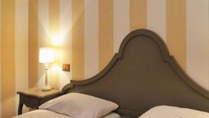 A hotel room with a striped wall, a bed with white pillows, and a nightstand with a lamp. - Al Ponte B&B (Padova)
