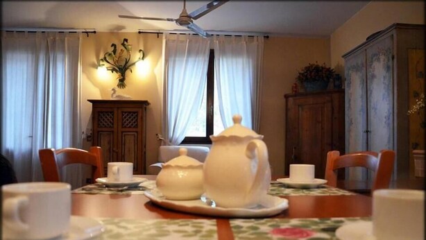 A dining area with a table set for tea, surrounded by chairs, a cabinet, and a ceiling fan. - Al Ponte B&B (Padova)
