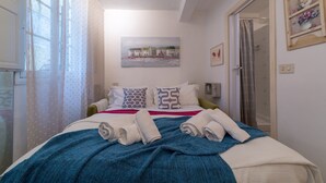 Un lit bien fait, avec des serviettes pliées, une couverture bleue et des coussins à motifs.