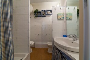 Kylpyhuoneessa on valkoinen pesuallas, kaksi wc-istuinta, suihku ja peili.