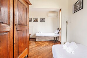 A hotel room with a wooden wardrobe, a bed with white bedding, a small bedside table, and a floor lamp.