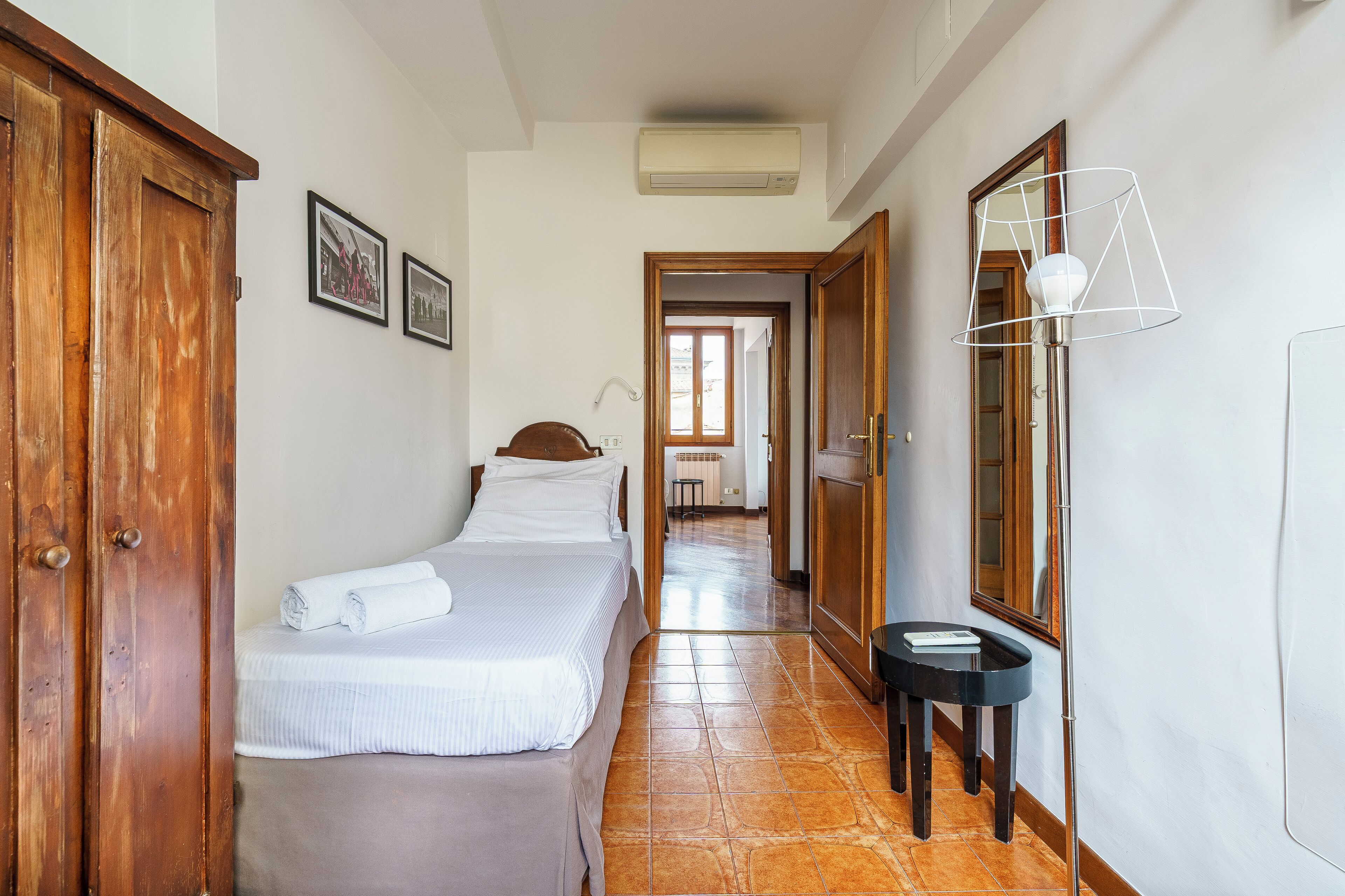 A hotel room with a bed, a bedside table, a mirror, and a door.