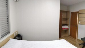 Un dormitorio con cama, escritorio, silla, televisor montado en la pared y armario.