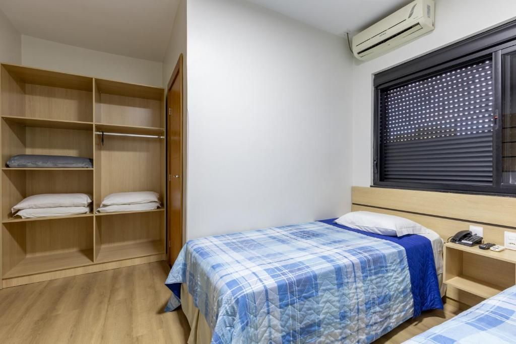 A bedroom with a bed, a wardrobe, a window with blinds, and an air conditioning unit.